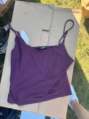 Mörkrött linne från BikBok - Säljer en enkel och snygg mörkrött linnetopp från BikBok. Toppen har tunna axelband och är croppad i modellen, perfekt till sommaren. Materialet känns mjukt och stretchigt, troligen bomull eller polyester. Passar till allt från jeans till kjol.