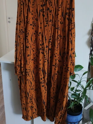 Lång leopardmönstrad klänning Vila - Säljer en lång klänning från Vila i en snygg orange-brun ton med svart leopardmönster. Klänningen har långa ärmar och knappar framtill. Perfekt för dig som vill sticka ut med ett djurmönstrat plagg!