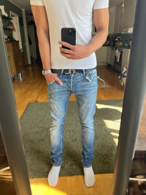 Slitna slim fit jeans - Säljer ett par ljusblå slim fit jeans med klassisk femficksdesign och snygga slitningar. Jeansen har låg midja och smal passform som sitter tajt längs benen. Perfekta för dig som gillar en modern och avslappnad stil.