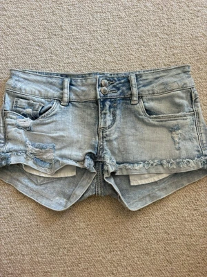 Ljusblå slitna jeansshorts - Säljer ett par ljusblå jeansshorts från tally weijl med fransig kant och slitna detaljer framtill och baktill. Shortsen har fem fickor, bälteshällor och dubbla knappar i midjan. Perfekta för varma dagar och en avslappnad stil.💓