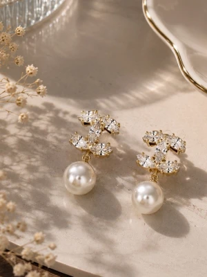 Guldörhängen med pärlor och kristaller - Eleganta örhängen i guldton med gnistrande kristaller formade som ett C-mönster och stora vita pärlor som hänger nedtill. Perfekta för dig som vill ha en lyxig och trendig accessoar med exklusiv känsla. Materialet ser ut att vara metall, kristall och pärlimitation.