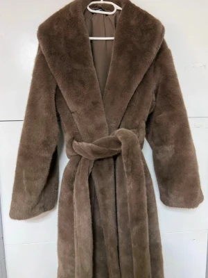 Kappa med knytskärp  - Säljer denna slutsålda fina långa pälsjackan med knytskärp i midjan. Jackan är brun och har oversize fit. Den har fluffigt material, sjalkrage, långa ärmar, fickor i sidorna och hysk och hakestängning framtill. Nytt skick, inte kommit till användning Kika gärna in mina andra artiklar för bundle rabatt!🌸