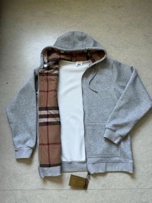 Burberry zipper - Burberry Vit Zip Hoodie – Strl M  Säljer en vit Burberry zip hoodie i storlek M. Helt ny och oanvänd, i perfekt skick.  • Bra kvalitet och bekväm. • Stilren och tidlös design som passar till alla tillfällen. • Mjuk passform med dragkedja och huva.  Hör gärna av dig vid frågor eller om du vill ha fler bilder.