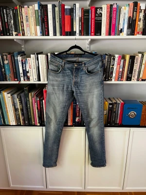 Blå slitna jeans med raka ben - Säljer ett par klassiska blå jeans med raka ben och fem fickor. Jeansen har en snygg sliten tvätt och kontrastsömmar på bakfickorna. Tillverkade i denim med en autentisk vintagekänsla. Perfekta för en avslappnad och trendig look.