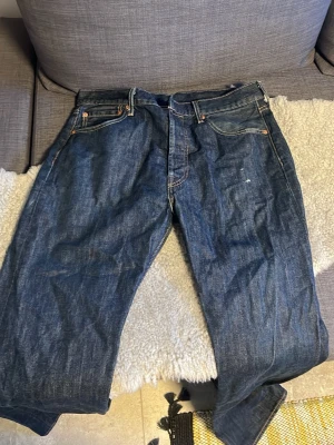 Mörkblå raka 501s från Levis - Säljer ett par klassiska mörkblå jeans med raka ben och fem fickor från Levis. Jeansen har kontrastsömmar och en patch bak i midjan. Perfekta till vardagslooken och tillverkade i slitstarkt denimtyg. Lite distressing vid ena låret men annars är det i perfekt skick, jätte sköna och passar dig som vill ha schyssta jeans. Hör av dig vid minsta fundering!!