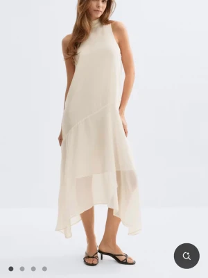 Ljus långklänning med knyt i nacken - Säljer en elegant ljus långklänning i ett tunt, svepande material. Klänningen är ärmlös, har hög hals och ett snyggt knyt i nacken. Asymmetrisk nederkant ger en modern touch. Perfekt för sommarens alla tillfällen. Aldrig använt helt ny. Den har tvättats en gång. Säljer eftersom att den inte riktigt är min stil💕 Ordinarie pris var 500kr 