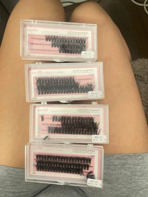 Mixade svarta lösögonfransar i knippen - Säljer fyra askar med mixade svarta lösögonfransar i knippen. Fransarna är i olika längder och tjocklekar, perfekta för att skapa en personlig look. Förpackningarna är genomskinliga med rosa bakgrund och fransarna är av syntetmaterial.