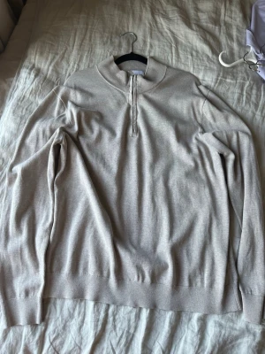 Beige halvzip tröja i bomull - Snygg beige långärmad tröja med halvzip och ribbade muddar. Tröjan har en hög krage som kan bäras både uppvikt och nedvikt. Tillverkad i mjuk bomull, perfekt för lager på lager och enkel att matcha med olika outfits.