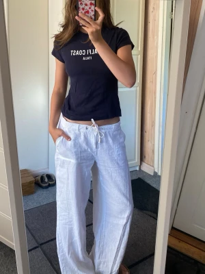 Blå t-shirt med Amalfi Coast-tryck - Blå t-shirt med vitt tryck där det står 'AMALFI COAST ITALIA' på bröstet. Modellen är klassisk med rund hals och korta ärmar. Perfekt till jeans eller linnebyxor för en chill vibe.