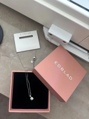 Edblad Leonore halsband i stål - Snyggt halsband från Edblad, modell Leonore, i rostfritt stål. Kedjan är silverfärgad och har ett hängsmycke med en klar, gnistrande pärla. Kommer i original ask och är perfekt för dig som gillar stilrena accessoarer.