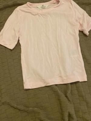 Ljusrosa t-shirt från H&M - Enkel och stilren ljusrosa t-shirt från H&M. T-shirten har korta ärmar och är gjord i mjuk bomull, perfekt för en avslappnad look. Passformen är normal och färgen är diskret och lättmatchad.