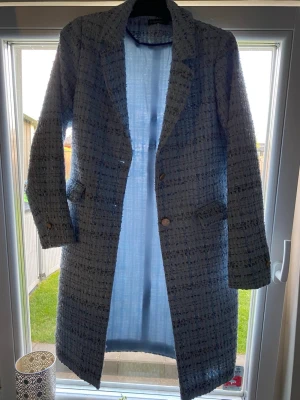 Ljusblå tweedkappa från Soulmate - Snygg ljusblå kappa i tweed från Soulmate. Kappan har klassisk krage, två fickor framtill och stängs med knappar. Materialet är strukturerat och ger en trendig look. Perfekt för dig som vill sticka ut med en stilren och modern kappa.