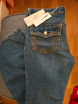 Gina jeans ultra low flap  - Aldrig använt!! Säljer pg fel storlek. Snygga blå jeans med markerade orange kontrastsömmar och en unik bakficka med lock och knapp. Klassisk femficksmodell i denim med raka ben. Perfekta för en avslappnad och trendig stil. Ultra low också 🥰
