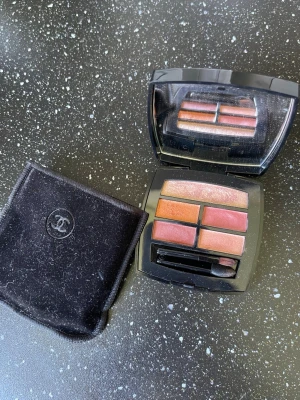 Chanel Les Beiges ögonskuggspalett - Snygg ögonskuggspalett från Chanel Les Beiges med fyra nyanser i varma toner som guld, koppar och rosa. Kommer i en elegant svart dosa med spegel och applikator samt en svart sammetsfodral med Chanel-logga. Perfekt för att skapa naturliga eller glamorösa looks.
