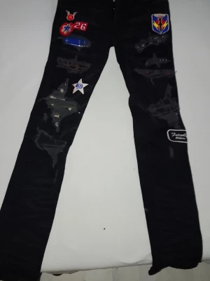 Amiri Jeans, bra skick, svarta storlek 32 - Säljer ett par svarta jeans från Amiri med flera coola patches och slitningar. Jeansen har raka ben och detaljer som stjärnor, märken och broderade lappar. Perfekta för dig som vill sticka ut med en unik streetwear-look.