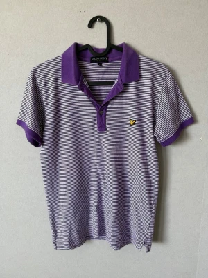 LYLE & SCOTT pikétröja - Snygg pikétröja i lila och vitt med smala ränder och klassisk krage. Tröjan har korta ärmar, knäppning framtill och en gul logga på bröstet. 