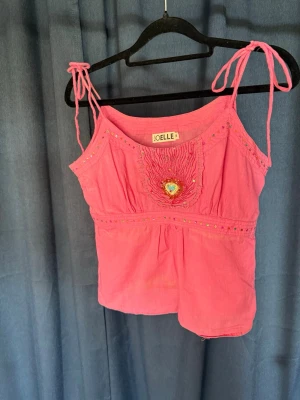 Rosa linnetopp med broderat hjärta - Söt rosa linnetopp från Joelle med knytband på axlarna och broderat hjärta framtill. Toppen har små paljettdetaljer och är perfekt för varma dagar. Lätt och luftig känsla med fina färgglada detaljer. Lite blekt i tyget men inget som man riktigt tänker på! 