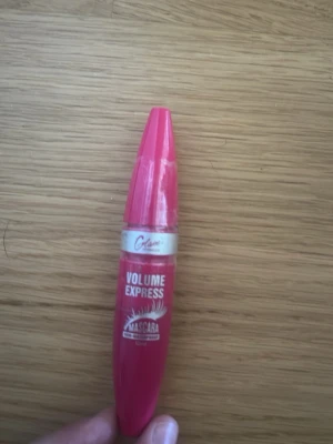 Rosa Volume Express mascara - Säljer en rosa Volume Express mascara med vit text och silvrig detalj på hylsan. Tuben har en avlång, droppformad design och är tillverkad i plast. Perfekt för dig som vill ha fylliga fransar och en snygg look.