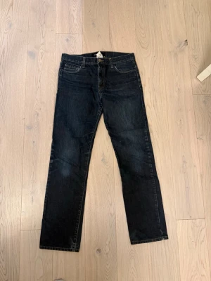 Mörkblå raka jeans från J.Lindeberg - Snygga mörkblå jeans från J.Lindeberg med raka ben och klassisk femficksmodell. Jeansen har kontrastsömmar och en liten JL-logga på myntfickan. Perfekta till en avslappnad stil och tillverkade i denim. Lite slitna och påväg till hål i skrevet W29 L32