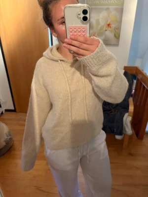 Beige stickad hoodie med huva - Mysig beige stickad hoodie med luva och dragsko. Tröjan har en avslappnad passform, långa ärmar och ribbade muddar vid ärmslut och nederkant. Säljs inte längre på Gina💞