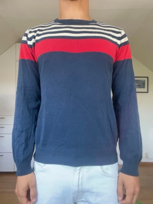Marinblå stickad tröja med ränder - Marinblå tröja från gant med röda och vita ränder tillverkad i 100% bomull. Strl S. Inga defekter. Modellen är 178 cm och väger 77 kg. Hör gärna av dig vid frågor!