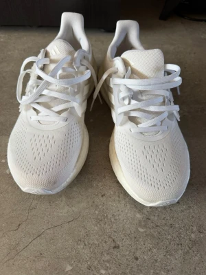 Vita Adidas sneakers med mesh - Säljer ett par fräscha vita Adidas sneakers med klassiska tre ränder på sidan. Ovandelen är i ventilerande mesh och sulan är tjock och bekväm. Skorna har lågt skaft och vita snören. Perfekta för dig som gillar stilrena och sportiga sneakers. Stl 42 2/3