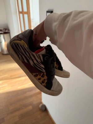 Zebra- och leopardmönstrade sneakers - Unika sneakers från Zadig & Voltaire med coolt zebra- och leopardmönster i svart, vitt och brunt. Skorna har svarta snören, gulddetaljer och en vit sula. Perfekta för dig som vill sticka ut med din stil.