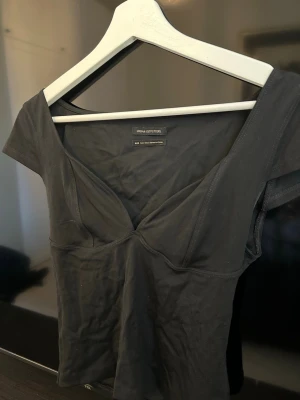 Svart topp från Urban Outfitters - Snygg svart topp från Urban Outfitters med djup v-ringning och korta ärmar. Toppens passform är figurnära och materialet känns mjukt och stretchigt, perfekt för en trendig och enkel look.