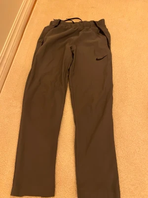 Gråa Prazzelbyxor från Nike - Snygga gråa mjukisbyxor från Nike med svart logga på vänster ben. Byxorna har resår i midjan med dragsko och raka ben. Perfekta för chill eller träning. Mjukt och bekvämt material med fickor på sidorna.