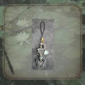 Phone Charm/Bagcharm - Butterfly Bloom - Guld, Silver & Grön - 🦋🌿 Fairycore- & Butterflycore-inspirerad phone charm/bagcharm med fjäril, blomma och glittrande detaljer i mintgrönt, silver och ljusa toner. En mjuk och sagolik design med naturinspirerad känsla. ✨  ౨ৎ ˖ ࣪⊹•⊹₊ ⋆୨ৎ  Handgjort av mig.  Frågor? Skicka bara. Kolla noggrant innan köp och klicka in på fotona. Returer av smycken godkänns ej av hygienskäl.