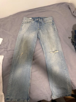 Ljusblå slitna jeans från Zara - Ljusblå jeans från Zara med raka ben och snygga slitningar på båda benen. Jeansen har klassisk femficksdesign och är tillverkade i bomull. Perfekta för en avslappnad och trendig look.