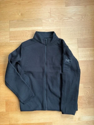 Arcteryx fleece  - Svart fleecejacka med hel dragkedja framtill och hög krage. Jackan har långa ärmar och diskret logga på vänster ärm. Storleken är medium men inte passar absolut bäst för storlek s 