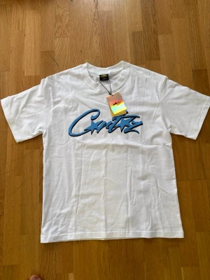 Corteiz t shirt - Säljer en vit t-shirt i bomull med ett stort blått grafiskt tryck på bröstet där det står 'Cartz' i streetstil. Klassisk rund hals och korta ärmar. Perfekt för dig som gillar enkel men snygg design. (Behöver bara strykning😀)