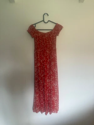  Beautiful red flowery sundress with a slit  S  - Snygg röd långklänning med vita blommor och offshoulder-modell. Klänningen har korta ärmar och ett smockat liv som ger en bekväm passform. Perfekt för sommarens alla tillfällen.