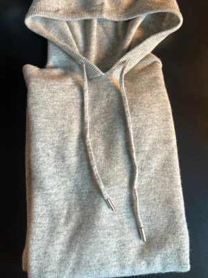 Ljusgrå Kashmir hoodie - Snygg ljusgrå hoodie i mjuk Kashmir material med klassisk huva och dragsko med silverfärgade detaljer. Perfekt för en  avslappnad stil. Hoodien har en enkel och stilren design utan tryck eller logga. SHIPPING ON SAME DAY!