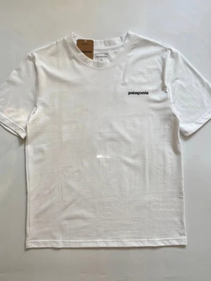 Vit t-shirt från Patagonia - Snygg vit t-shirt från Patagonia med liten svart logga på bröstet. Klassisk rund halsringning och korta ärmar. Tillverkad i mjuk bomull som känns skön mot huden. Perfekt för en clean och stilren look.