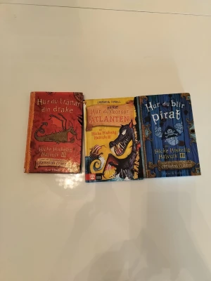 Hur du tränar din drake-bokpaket - Ett paket med tre färgglada böcker ur serien om Hicke Hiskelig Halvulk III av Cressida Cowell. Omslagen är i rött, gult och blått med illustrationer av drakar och pirater. Perfekt för dig som gillar äventyr och fantasy.  Böckerna i paketet: Hur du blir pirat, Hur du korsar Atlanten, Hur du tränar din drake