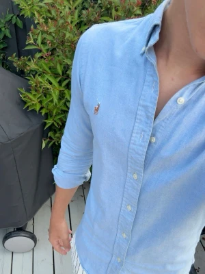 Blå Ralph Lauren Skjorta Slim Fit - Snygg ljusblå oxfordskjorta från Ralph Lauren i slim fit-modell. Skjortan har klassisk krage, knäppning framtill och broderad logga på bröstet. Tillverkad i stretchig bomull som ger en bekväm passform. Perfekt för en stilren look.