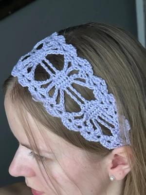 Ljuslila virkat hårband - Supersött ljuslila hårband som är virkat i ett unikt, blommigt mönster. Hårbandet är brett och har en luftig, bohemisk känsla. Perfekt för att piffa till frisyren och ge en romantisk touch till din look.