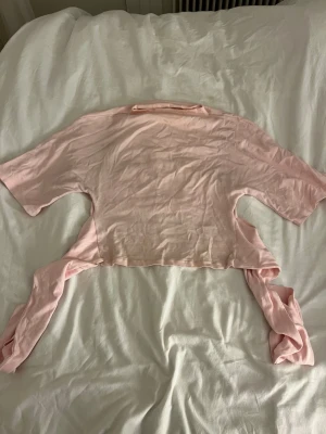 Ljusrosa croppad topp med knytband - Trendig ljusrosa topp från Gina . Tröjan är använd kanske 3 ggr men sömnen har fortfarande gått upp lite som man kan se på bild 3 !