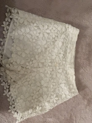 Vita spets-shorts med blommönster -  ett par  vita shorts med blommig spets. Perfekta för sommaren eller en utekväll. Köptes på sellpy men är från hollister. Jag har aldrig använt dem men syns att de är använda 