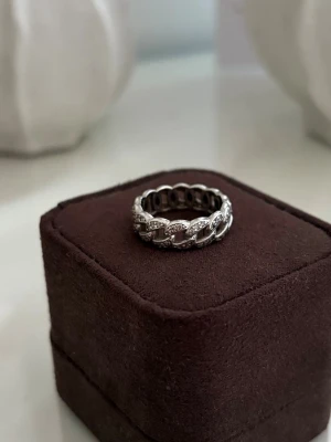 Silverfärgad kedjering med stenar - Snygg ring i silverfärg med ett kedjeformat band runt hela ringen. Ringen är dekorerad med små gnistrande stenar som ger extra bling. Materialet ser ut att vara metall med infattade stenar🫶🏼