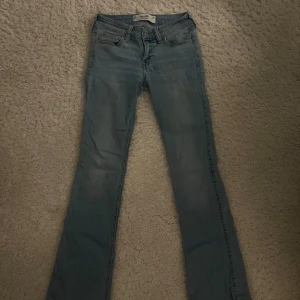 Bootcut jeans från Hollister ljusblå - Säljer ett par ljusblå bootcut jeans från Hollister med låg midja. Klassisk femficksmodell med snygga broderade detaljer på bakfickorna.  Innerbenslängden är 75 cm och midjan är 35 cm