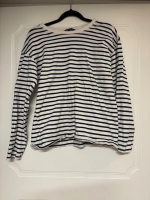 Randig långärmad tröja i bomull - Vit långärmad tröja med svarta horisontella ränder och rund halsringning. Tillverkad i mjuk bomull, perfekt för en avslappnad och stilren look. Klassisk passform med lätt avslappnad siluett.