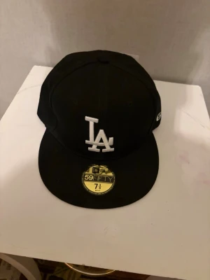 Svart LA-keps från New Era 59FIFTY - Svart keps från New Era 59FIFTY med LA Dodgers-logga broderad i vitt framtill och MLB-logga bak. Klassisk flat peak och strukturerad passform. Märke på sidan. Perfekt för dig som gillar streetwear och sportig stil.