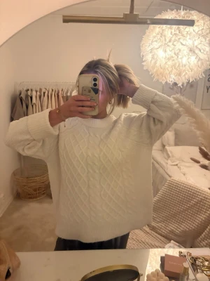 Vit kabelstickad tröja - Mysig vit kabelstickad tröja med hög hals och breda muddar. Tröjan har ett klassiskt flätmönster framtill och är lite oversized i modellen, perfekt för en avslappnad och trendig look.