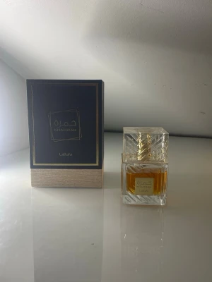 Lattafa Khamrah Eau de Parfum 100ml - Lattafa Khamrah Eau de Parfum i en elegant, fyrkantig glasflaska med gulddetaljer och genomskinligt lock. Den luktar som en nybakad äppelpaj och jag tycker den är lite för söt för mig. Doften kommer i en lyxig svart och guld kartong med träfärgad botten. Flaskan rymmer 100 ml jag skulle säga att det är runt 85 ml kvar, den har en exklusiv design som sticker ut på parfymhyllan.