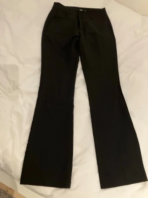 Svarta bootcut kostymbyxor Bik Bok storlek 34 - Snygga svarta kostymbyxor från Bik Bok med bootcut passform och hällor för skärp. Byxorna har klassisk design med raka ben och diskreta fickor. Perfekta för en clean och stilren look. Beninnelängd 80 cm midja 35 cm.
