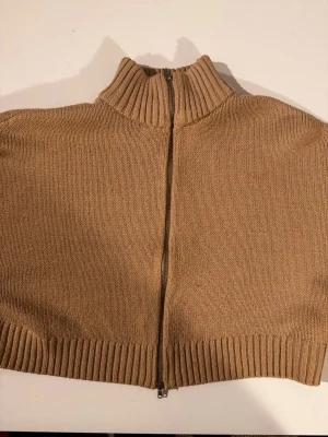 Beige stickad tröja med dragkedja  - Stickad tröja i beige med hög krage och hel dragkedja framtill. Tröjan har ribbstickade muddar vid hals, ärmslut och nederkant. Perfekt för lager på lager och enkel att matcha med olika outfits.