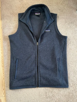 Patagonia väst - Snygg mörkblå fleeceväst från Patagonia med dragkedja framtill och två fickor med dragkedja. Västen har hög krage och är tillverkad i mjukt fleecematerial, perfekt för lager-på-lager och chill stil. Tveka inte att ställa frågor🤝